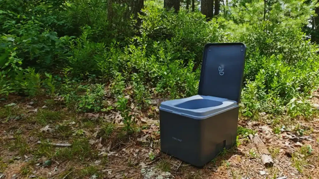 Compost toilet portátil colocado en un bosque, ideal para camping ecológico y gestión sostenible de residuos.